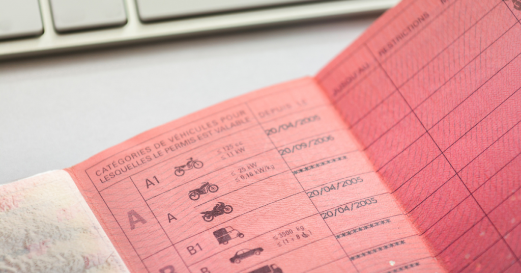 Een close-up van een roze, rijbewijs in papieren versie. Hij ligt open op tafel. En daarboven ligt een toetsenbord.