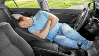 Man met blauwe t-shirt slaapt in een auto
