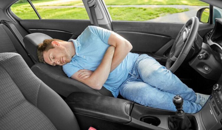 Man met blauwe t-shirt slaapt in een auto