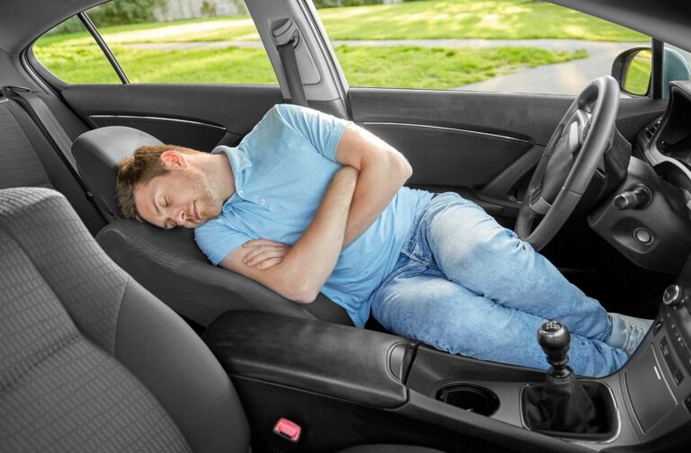 Man met blauwe t-shirt slaapt in een auto