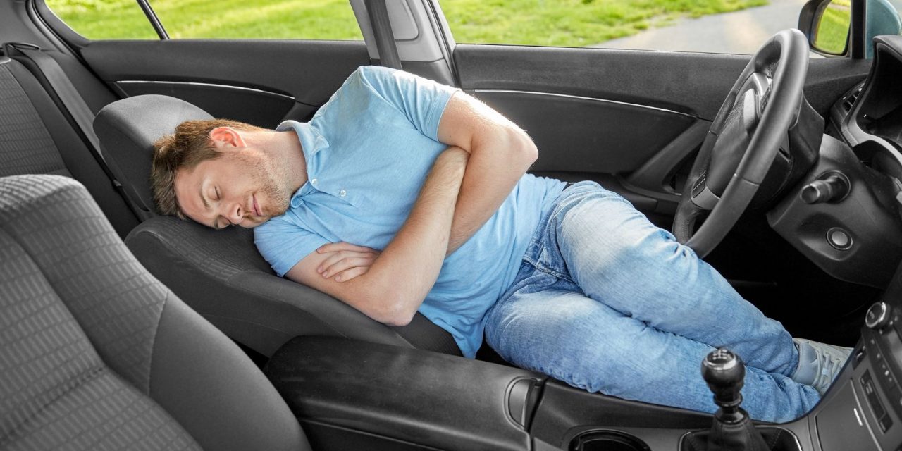 Man met blauwe t-shirt slaapt in een auto